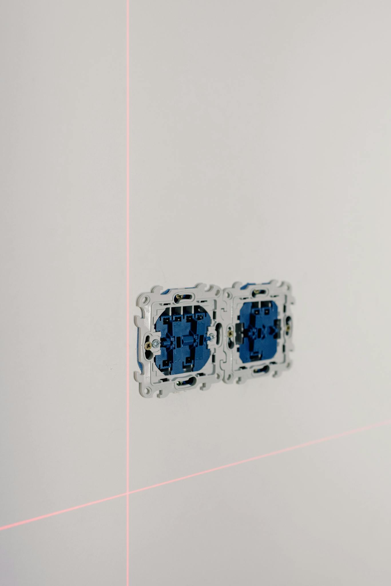 Close-up of an electrical socket installation with laser alignment lines in a minimalist interior.