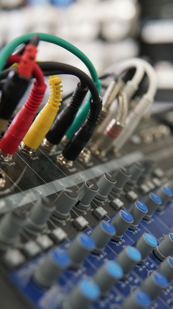 Anasayfa Detailed view of audio mixer controls and colorful connecting cords in a studio environment.